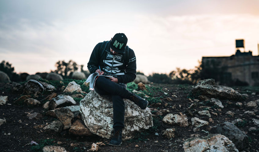 Menweer sits on a rock writing in his notebook