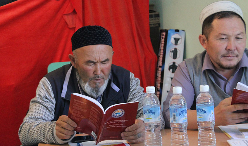 Two men sit at a desk reading training manuals. 