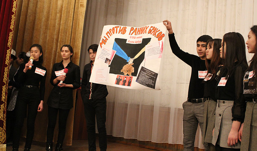 Students holding up a poster which says 'we are against early marriages'