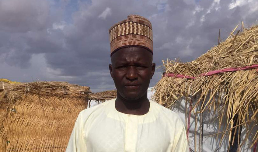 Yusuf Issa standing in front of dwellings in the displacement camp