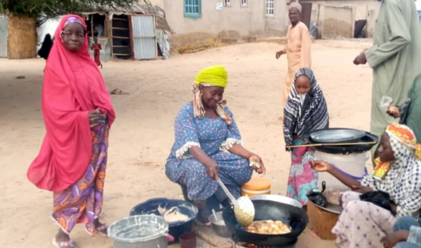 Woman cooking, others gathered around