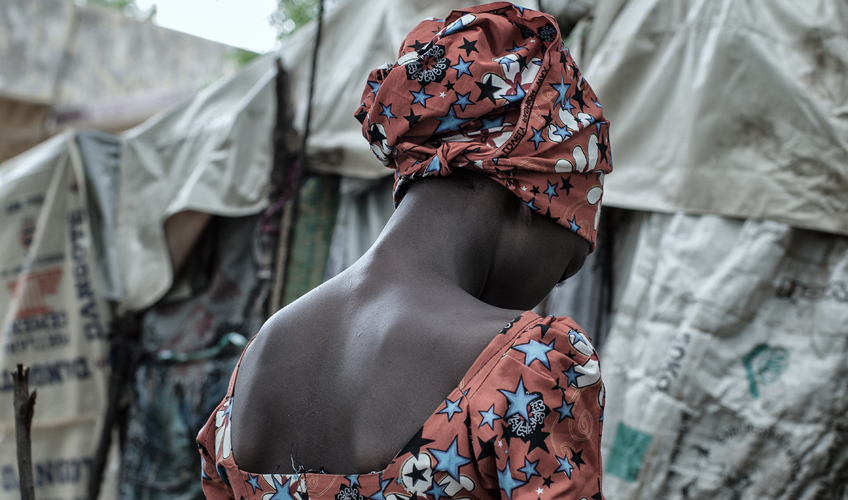 Kubili, wearing a floral dress and head scarf, photographed from the back.