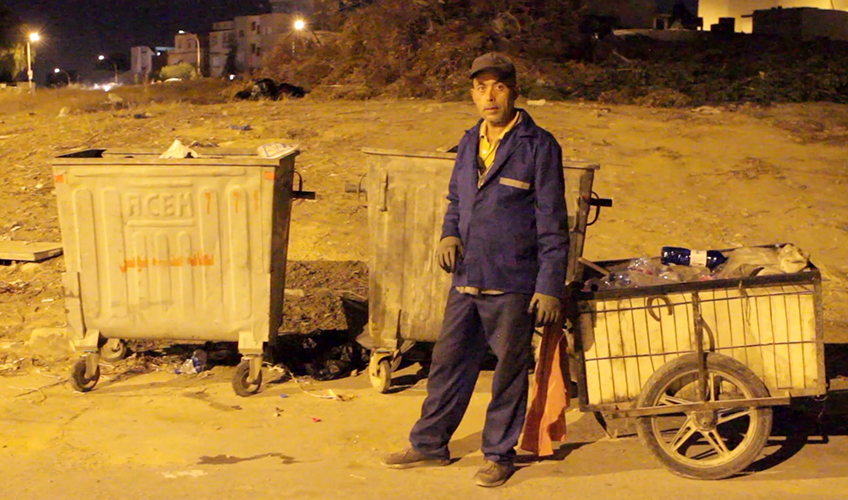 Fethi El-Chaaibi stands in front of his rubbish cart large near rubbish bins.