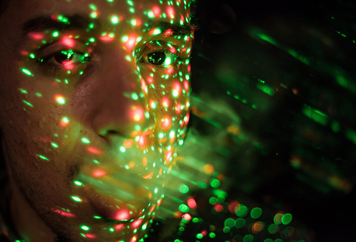 A young man stands with his mouth open as bright lights reflect on his face