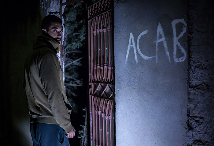 A young man stands by wall graffiti 