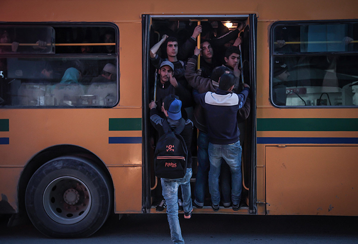 A young man tries to get onto a crowded bus, people crammed into the doorway