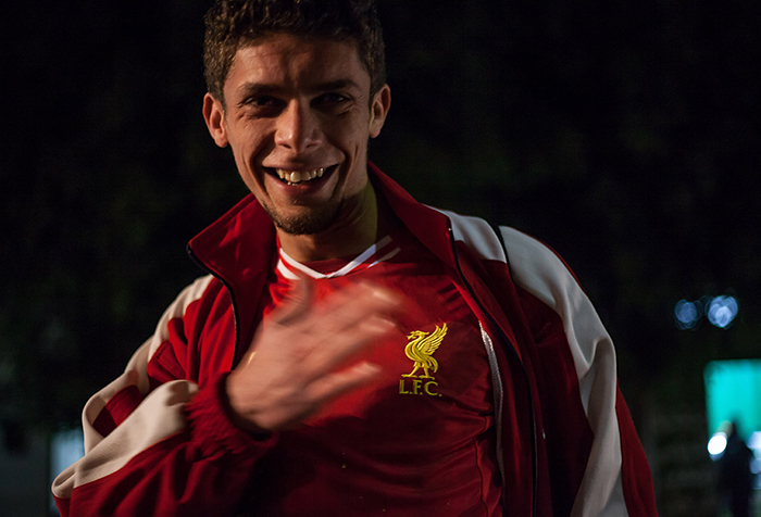 A young man smiles proudly while displaying his football shirt, hand on chest