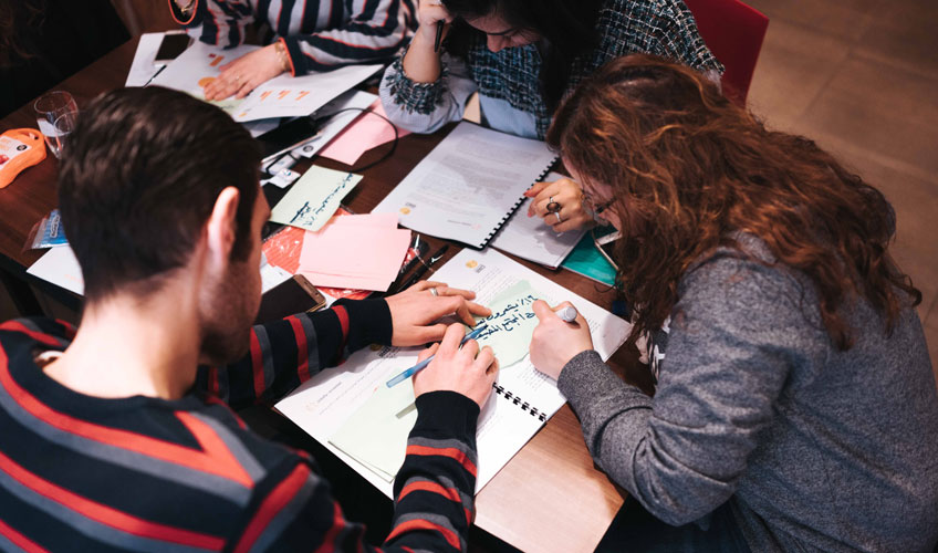 Rahaf and others bent over papers on a table.