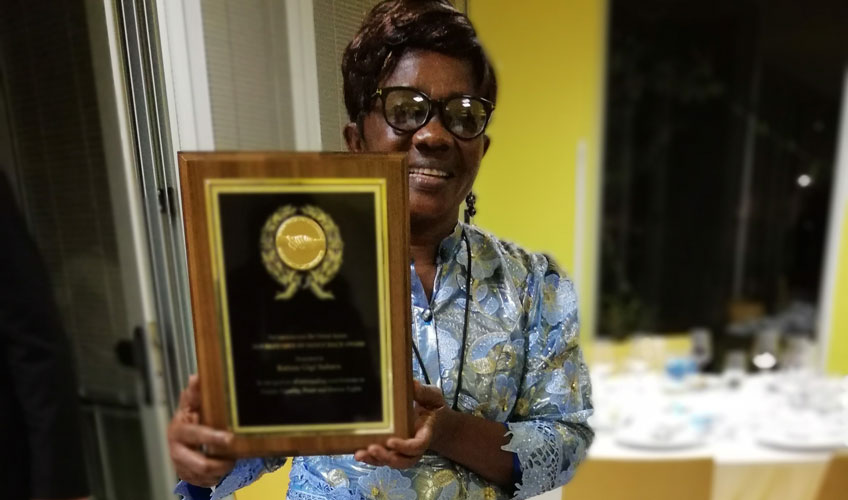 A Congolese woman smiles and holds up a wooden award plaque