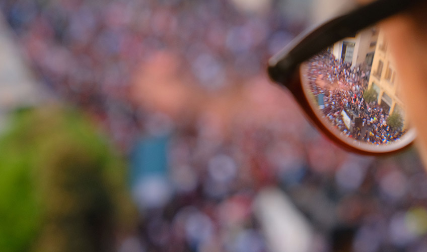 A person with glasses overlooks a  protest.