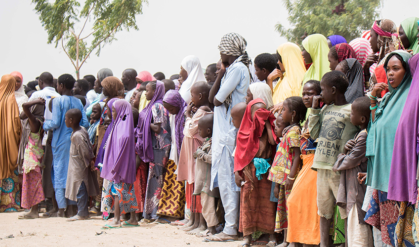 A group of African men, women and children wait in a line