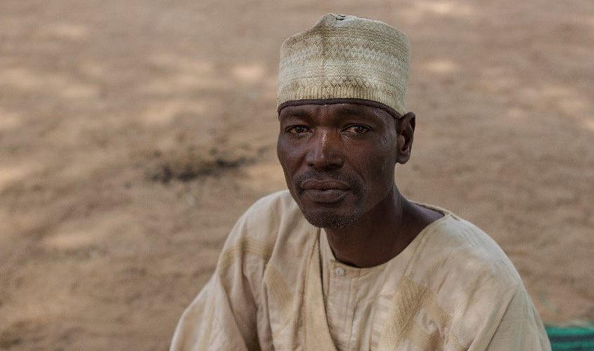 Portrait of Abdullahi, wearing a cream-coloured cap and robe