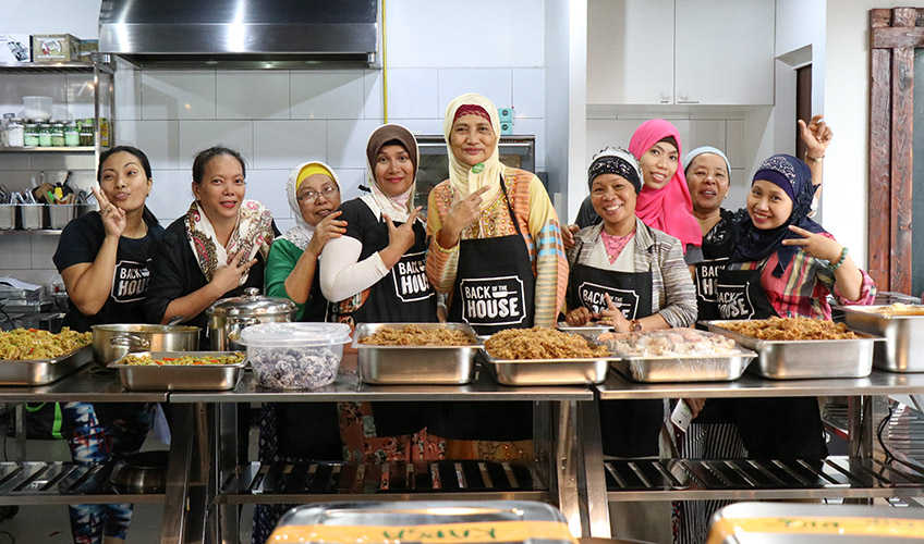 A group of smiling Filipino women gesture in front of prepared food