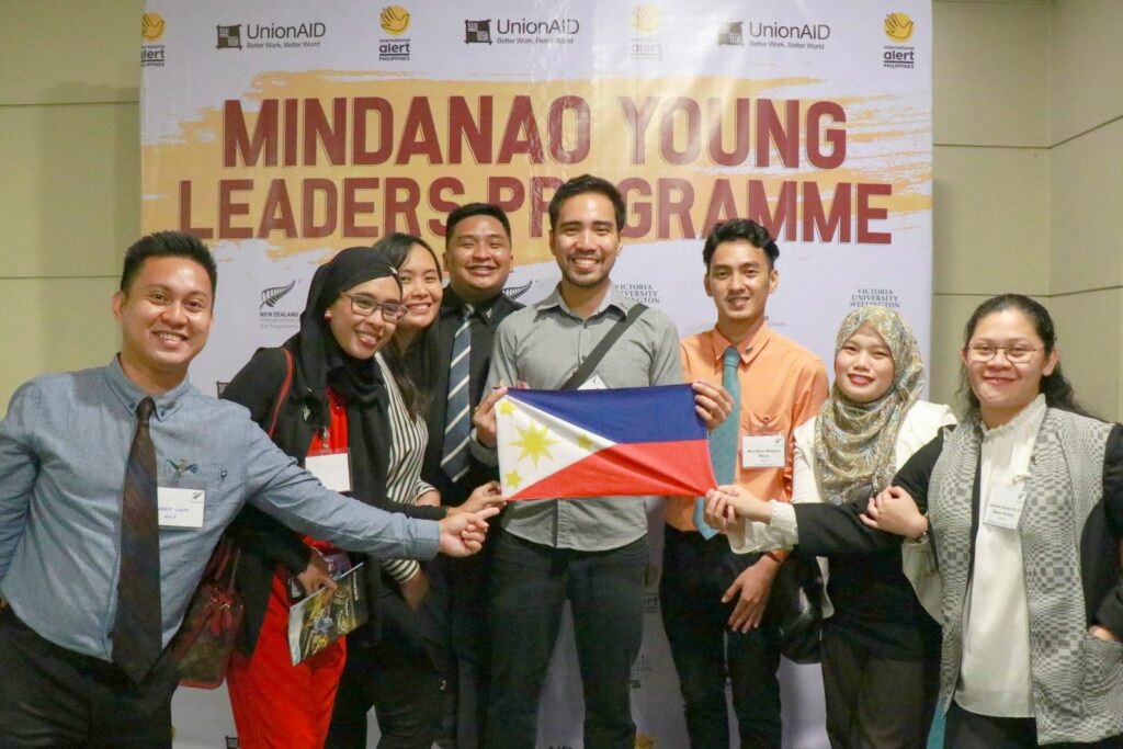 A group of young Filipino youth smile while holding their national flag