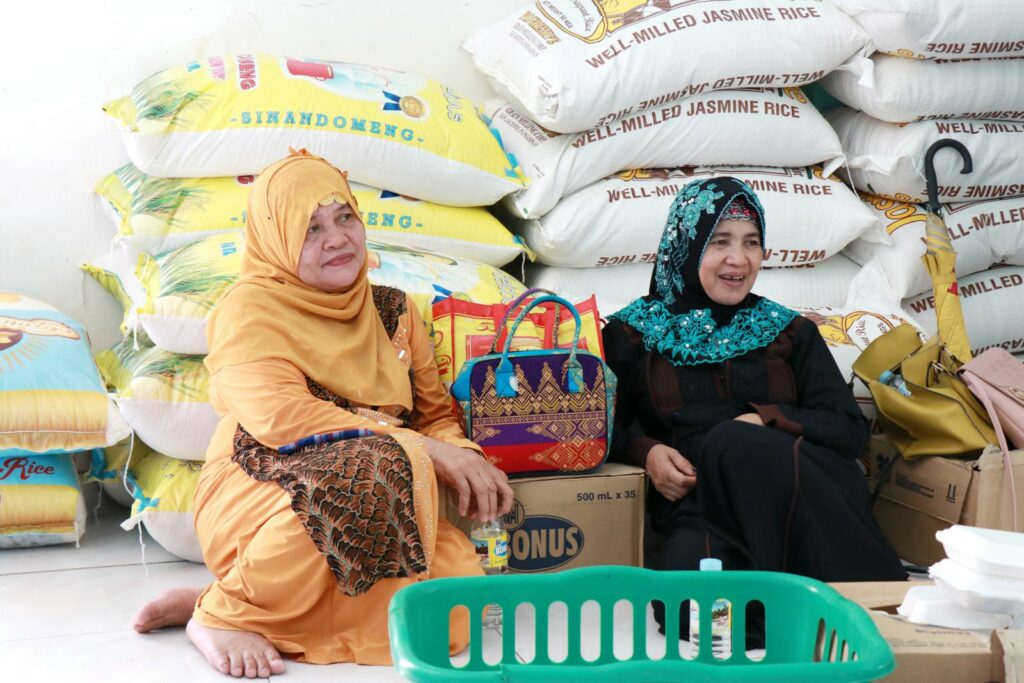 Two Filipino women smile while sitting in front of rice bags 