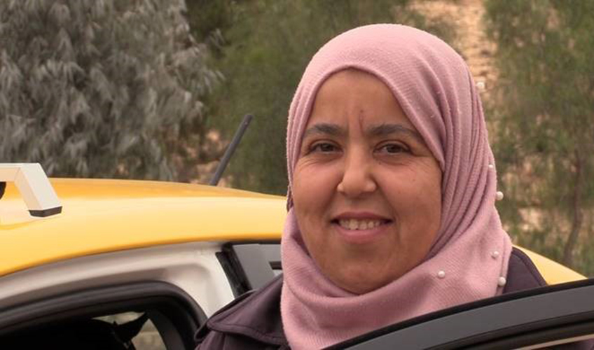 A Tunisian woman smiles while standing next to a car